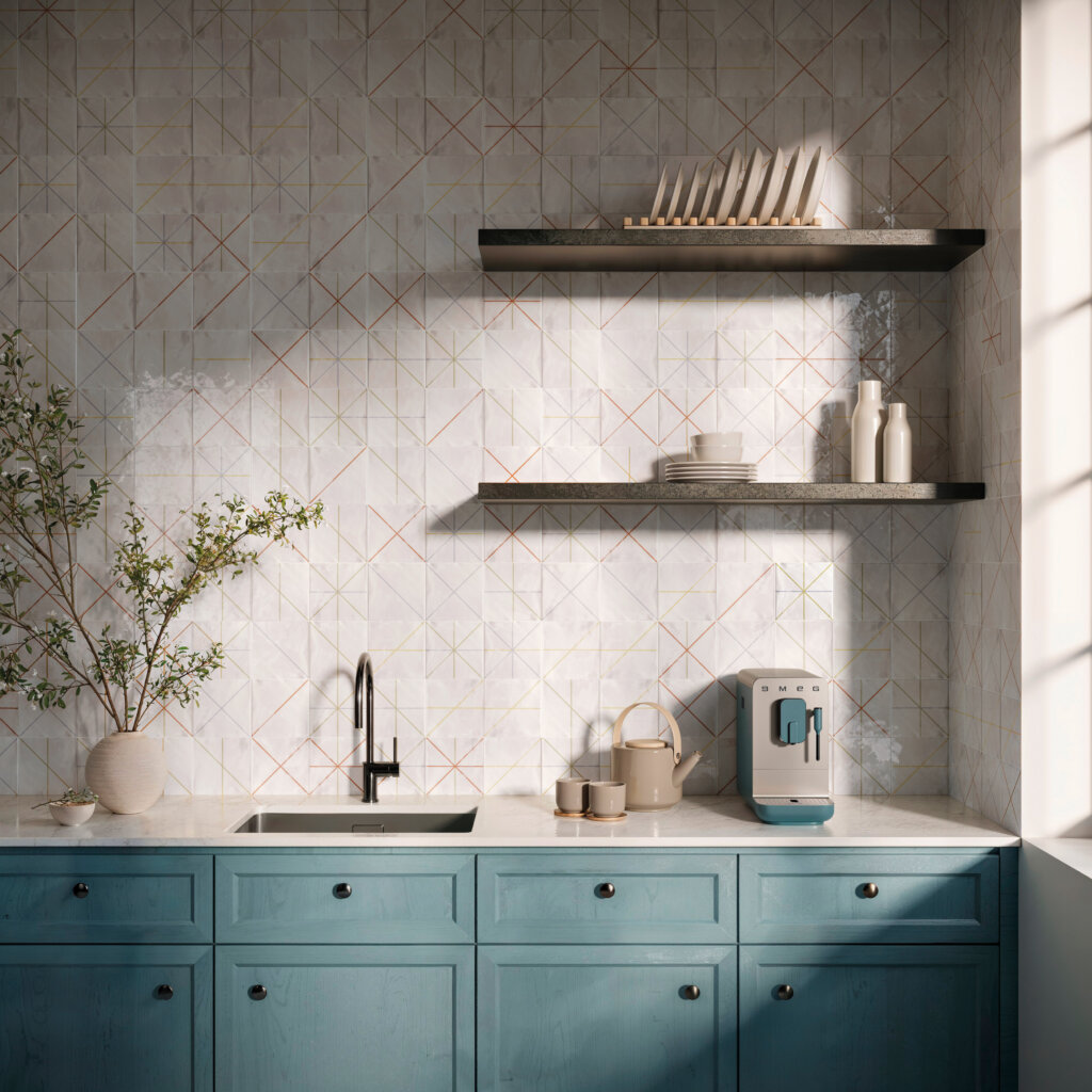 Cozinha contemporânea com rodabanca revestida com azulejos cerâmicos claros em formato quadrado (15.5x15.5 cm), decorados com delicados padrões geométricos em linhas coloridas inspiradas na renda de filé. Abaixo, bancada com pia e armários em tom azul-fechado.