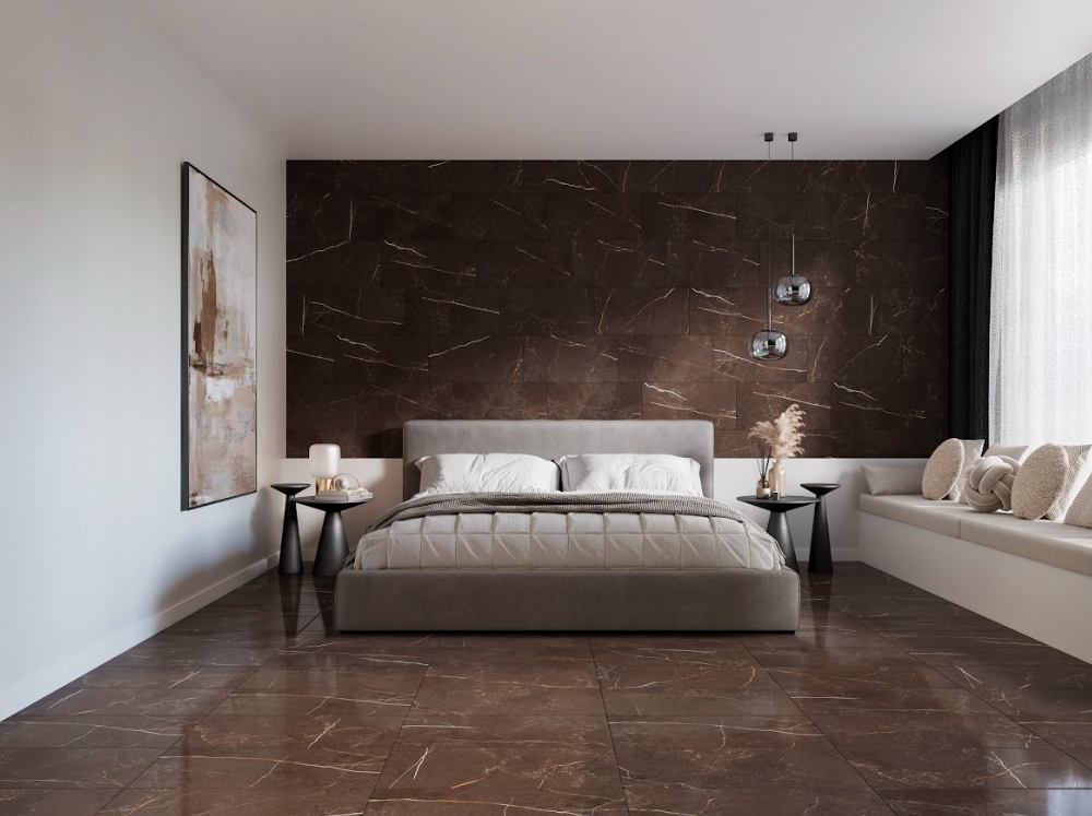 Quarto moderno com piso e parede de cabeceira revestidos com cerâmica escura que imita mármore marrom com veios claros. No centro, uma cama de casal cinza com enxoval claro.