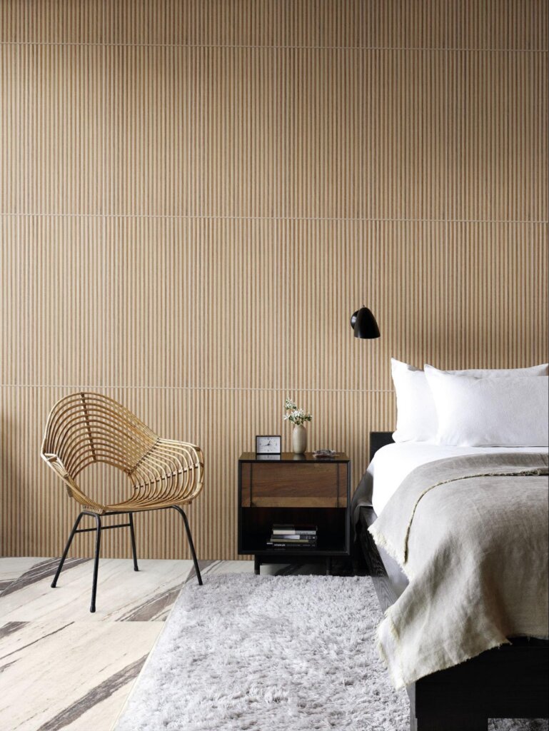 Quarto rústico-chic com parede de cerâmica ripada amadeirada, poltrona de fibra natural (rattan) e piso de mármore branco com veios escuros.